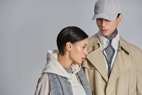 A young, stylish couple in trench coats posing confidently in a studio against a grey background. — Stock Photo