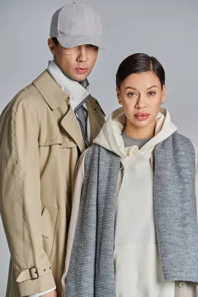 A young stylish couple wearing trench coats standing together in a studio against a grey background. - foto de stock