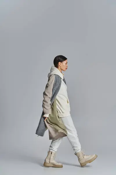 Eine junge, stylische Frau läuft selbstbewusst im Trenchcoat in einem Studio mit grauem Hintergrund. — Stockfoto