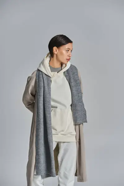 Une jeune femme élégante se tient avec confiance dans un trench coat sur un fond gris uni. — Photo de stock