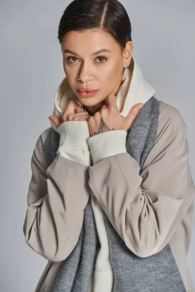 A young woman exudes style in a gray coat and white turtle neck sweater against a studios gray backdrop. — Stock Photo