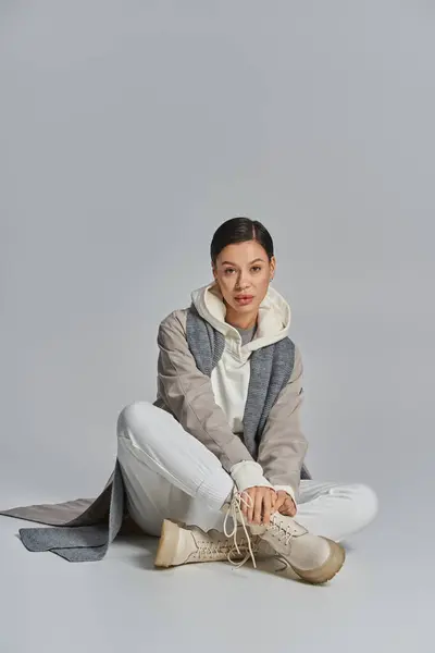 A chic young woman in a trench coat sits cross-legged on the ground, exuding a sense of calm and contemplation. — Stock Photo