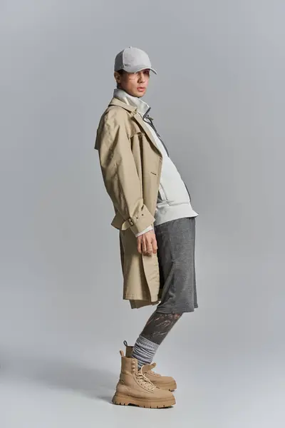 Ein stilvoller Mann posiert in Trenchcoat und Hut in einem Studio vor grauem Hintergrund. — Stockfoto