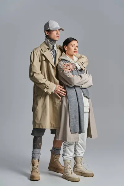 A stylish couple, dressed in trench coats, standing side by side in a studio against a grey background. — Stock Photo