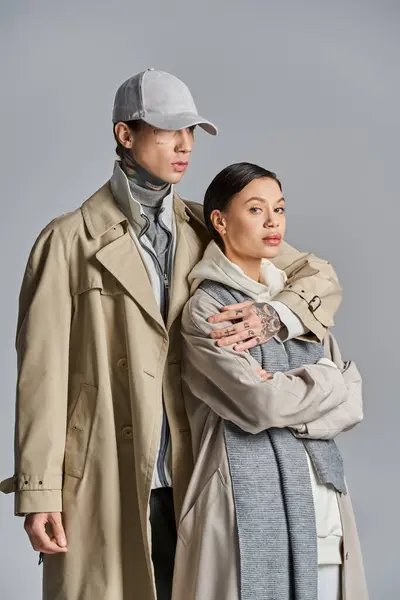 A young man and woman stand side by side in trench coats, exuding style and sophistication against a grey studio backdrop. — Stock Photo