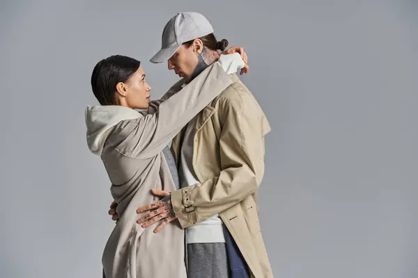A young, stylish couple standing side by side in trench coats against a grey studio background. — Stock Photo