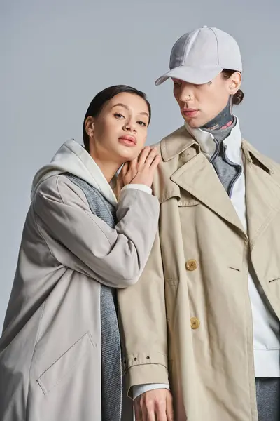 A young stylish couple stands confidently next to each other in trench coats against a grey studio background. — Stock Photo