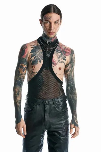 Um jovem com uma abundância de tatuagens adornando seu corpo posa confiantemente em um estúdio contra um fundo cinza. — Fotografia de Stock