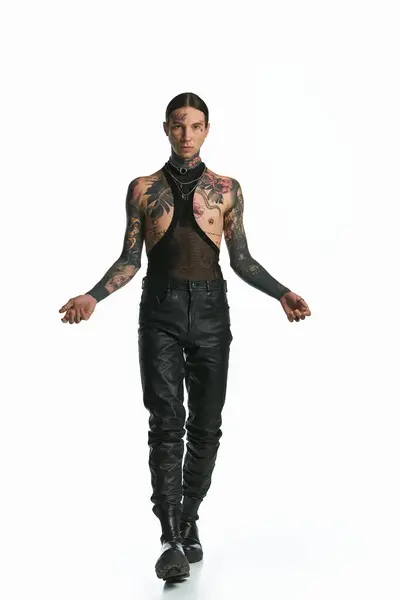 A stylish man covered in tattoos confidently walking down in a white studio setting. — Stock Photo