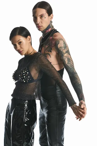 A stylish and tattooed young couple standing united against a grey backdrop in a studio. — Stock Photo