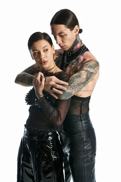 Una pareja joven y elegante, ambos tatuados, de pie juntos en un estudio sobre un fondo blanco. - foto de stock
