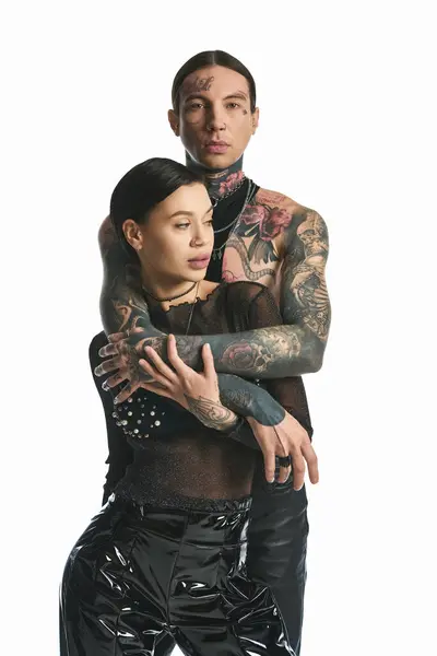 Una pareja joven y elegante con tatuajes intrincados en sus brazos posa en un estudio sobre un fondo gris. - foto de stock