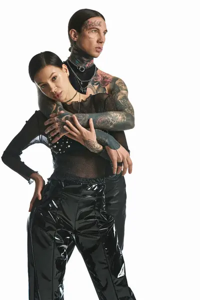 Un jeune couple élégant et tatoué vêtu de vêtements en latex pose dans un studio sur fond gris. — Photo de stock
