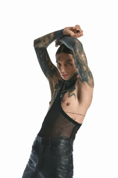 A young stylish man with tattoos strikes a pose in a studio on a grey background. — Stock Photo