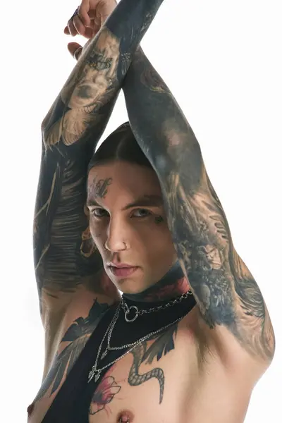 Молодой стильный мужчина с широкими татуировками и пирсингом на руках позирует в студии на сером фоне. — стоковое фото