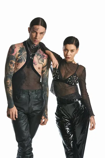 A young, stylish man and woman with tattoos stand together in a studio against a grey background. — Photo de stock