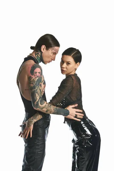 Стильний молодий чоловік і жінка, прикрашені татуюваннями, стоять разом у студії на сірому фоні. — стокове фото