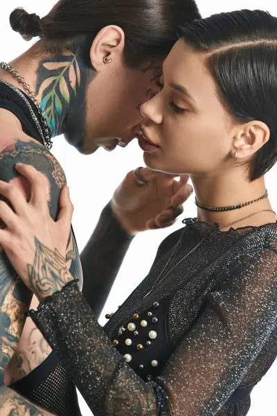Un couple élégant et tatoué enfermé dans un baiser passionné dans un studio sur fond gris. — Photo de stock