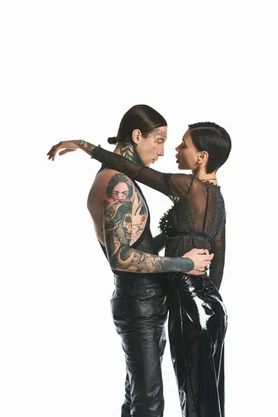 Ein stylisches und tätowiertes junges Paar, das sich in einem Studio vor grauem Hintergrund innig umarmt. — Stockfoto
