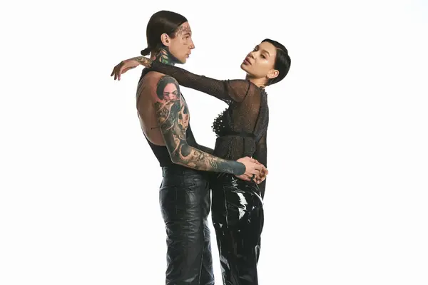 Un giovane uomo e una donna tatuati stanno fianco a fianco in uno studio, mettendo in mostra la loro intricata arte del corpo su uno sfondo grigio. — Foto stock
