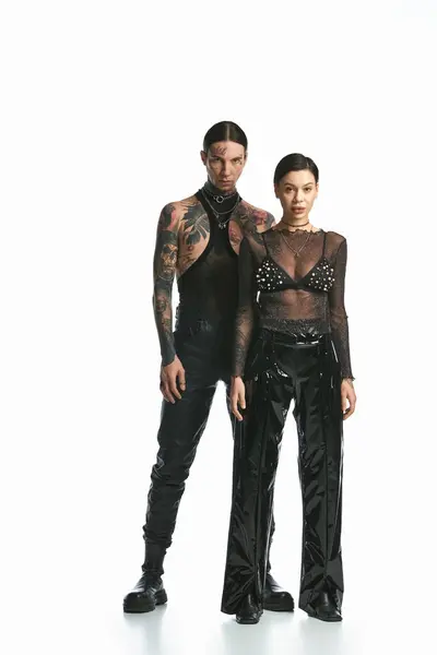 A young, stylish man and woman with tattoos stand next to each other in a photo studio against a grey background. — Stock Photo