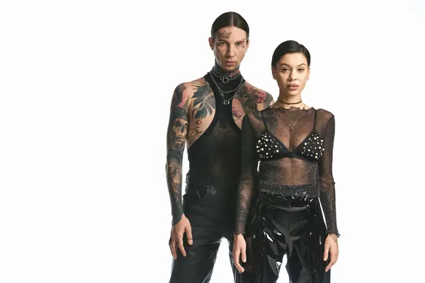 Um jovem casal elegante com tatuagens lado a lado em um estúdio contra um fundo cinza. — Fotografia de Stock