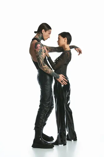 A young, stylish, and tattooed couple standing together in a studio against a grey background, showing affection and unity. — Stock Photo