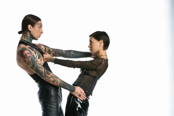 Una giovane coppia elegante con tatuaggi intricati sulle braccia in posa in uno studio su uno sfondo grigio. — Foto stock