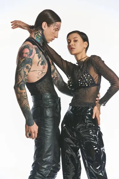 A stylish, tattooed young man and woman stand together in a studio against a grey background, exuding confidence and unity. — Stock Photo
