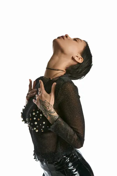Una giovane donna elegante con tatuaggi che indossa una camicia nera, catturata in uno studio su uno sfondo grigio. — Foto stock