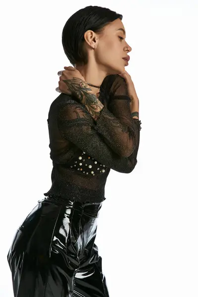 Une jeune femme en chemise noire et pantalon frappe une pose en studio, ornée de tatouages — Photo de stock