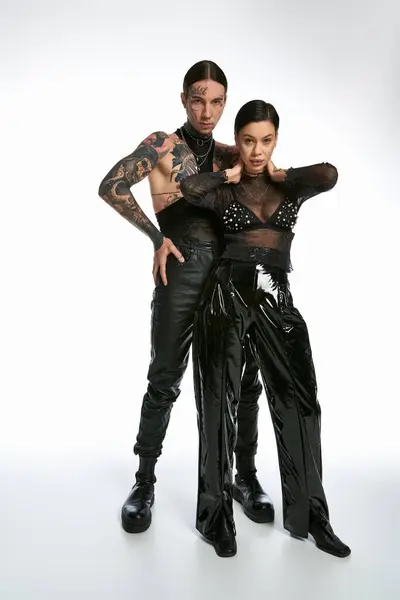 Una pareja elegante y tatuada se encuentra en un estudio sobre un fondo gris, mostrando unidad y afecto. - foto de stock