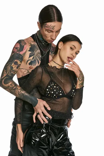 Un jeune homme et une jeune femme, élégamment habillés et tatoués, posant ensemble dans un studio sur un fond gris. — Photo de stock