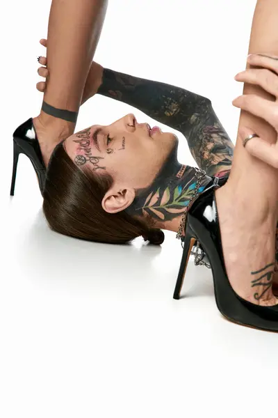 Молодая, стильная женщина на высоких каблуках с гордостью показывает замысловатые татуировки на ноге в студии на сером фоне. — стоковое фото