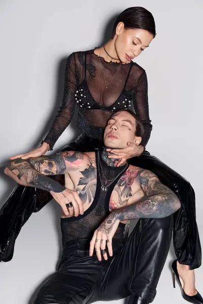 Un hombre y una mujer elegantes y tatuados posan en un estudio sobre un fondo gris. - foto de stock