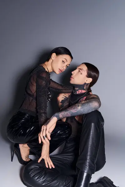 Молодой, стильный мужчина и женщина с татуировками сидят на полу в студии на сером фоне. — стоковое фото