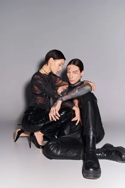 Un homme et une femme jeunes, élégants et tatoués assis ensemble sur un fond de studio gris. — Photo de stock
