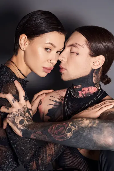 A stylish, tattooed couple sharing a warm hug in a studio against a grey background, expressing love and intimacy. — Stock Photo
