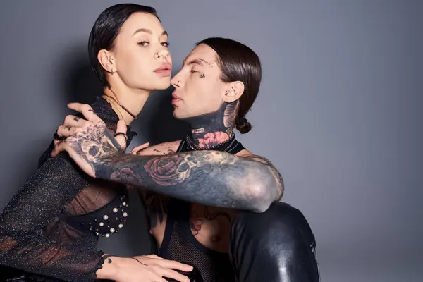 Um jovem, elegante, tatuado homem e mulher fazer uma pose em um estúdio contra um fundo cinza. — Fotografia de Stock
