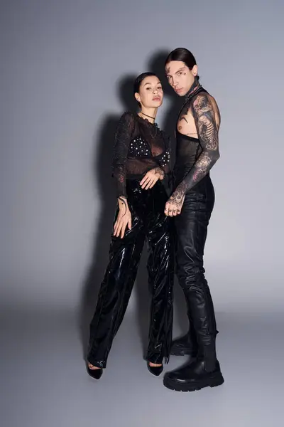 Two young, stylish women with tattoos standing side by side in a studio against a grey background. — Stock Photo