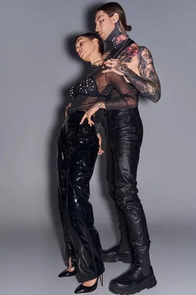 Молодая, стильная пара в черном с татуировками, позирующая в студии на сером фоне. — стоковое фото