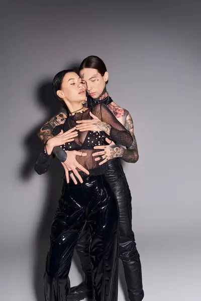 A young stylish couple with tattoos embrace each other warmly in a studio against a grey background. — Stock Photo