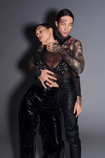 Ein junges, stylisches, tätowiertes Paar steht zusammen in einem Studio vor grauem Hintergrund. — Stockfoto