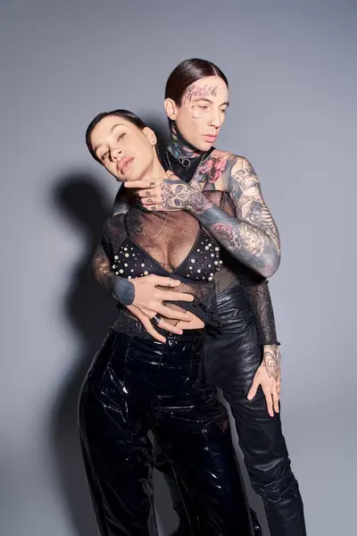 A young, stylish, tattooed couple posing gracefully in a studio against a grey background. — Stock Photo