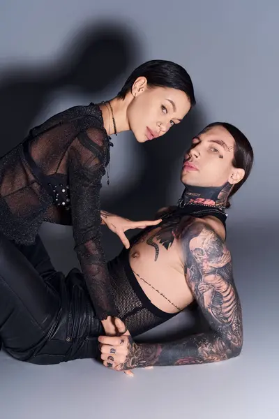 A stylish young man and woman with tattoos posing together in a studio against a grey background. — Stock Photo