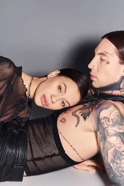 A young, stylish, and tattooed couple posing confidently in a studio on a grey background. — Stock Photo
