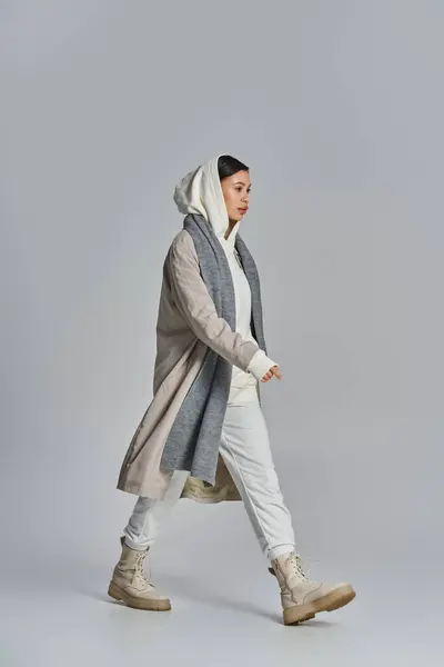 A stylish woman walking in a gray and white outfit within a studio setting. — Stock Photo