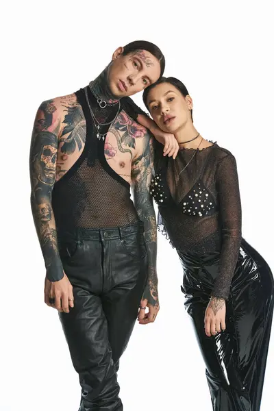 Un giovane uomo e una donna elegante e tatuati battono una posa insieme in uno studio su uno sfondo grigio. — Foto stock