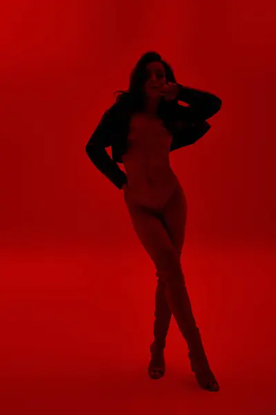 Jovem mulher confiantemente posa com as mãos nos quadris em uma sala vermelha vibrante. — Fotografia de Stock