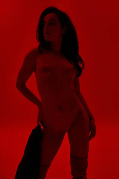 Giovane donna si alza con fiducia, mani sui fianchi, in vibrante stanza rossa. — Foto stock